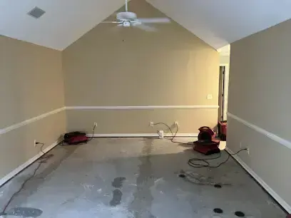 Empty room with a bare concrete floor and air movers running after the carpet came out