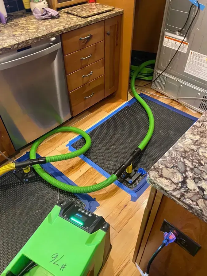 Extraction mat and hose drying hardwood in front of a kitchen dishwasher, appliance leak water damage in Goose Creek