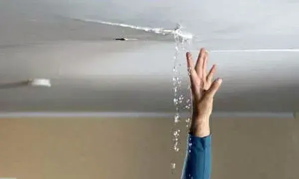 Water dripping from a crack in a white ceiling onto an outstretched hand, ceiling leak water damage in Goose Creek